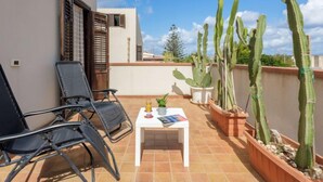 A balcony with two black chairs, a small table with a book and a glass, and several potted cacti. - Palma Gaia by Interhome (San Vito lo Capo)