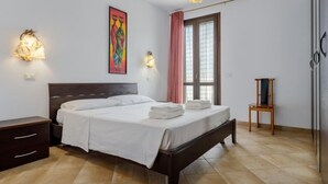 A bedroom with a bed, bedside tables, a chair, a window with curtains, and a painting on the wall. - Palma Gaia by Interhome (San Vito lo Capo)