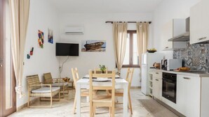 Ett modernt kök med vita skåp, en inbyggd ugn och en mikrovågsugn. Det finns en matplats med ett bord och stolar, och en tv som är monterad på väggen.
