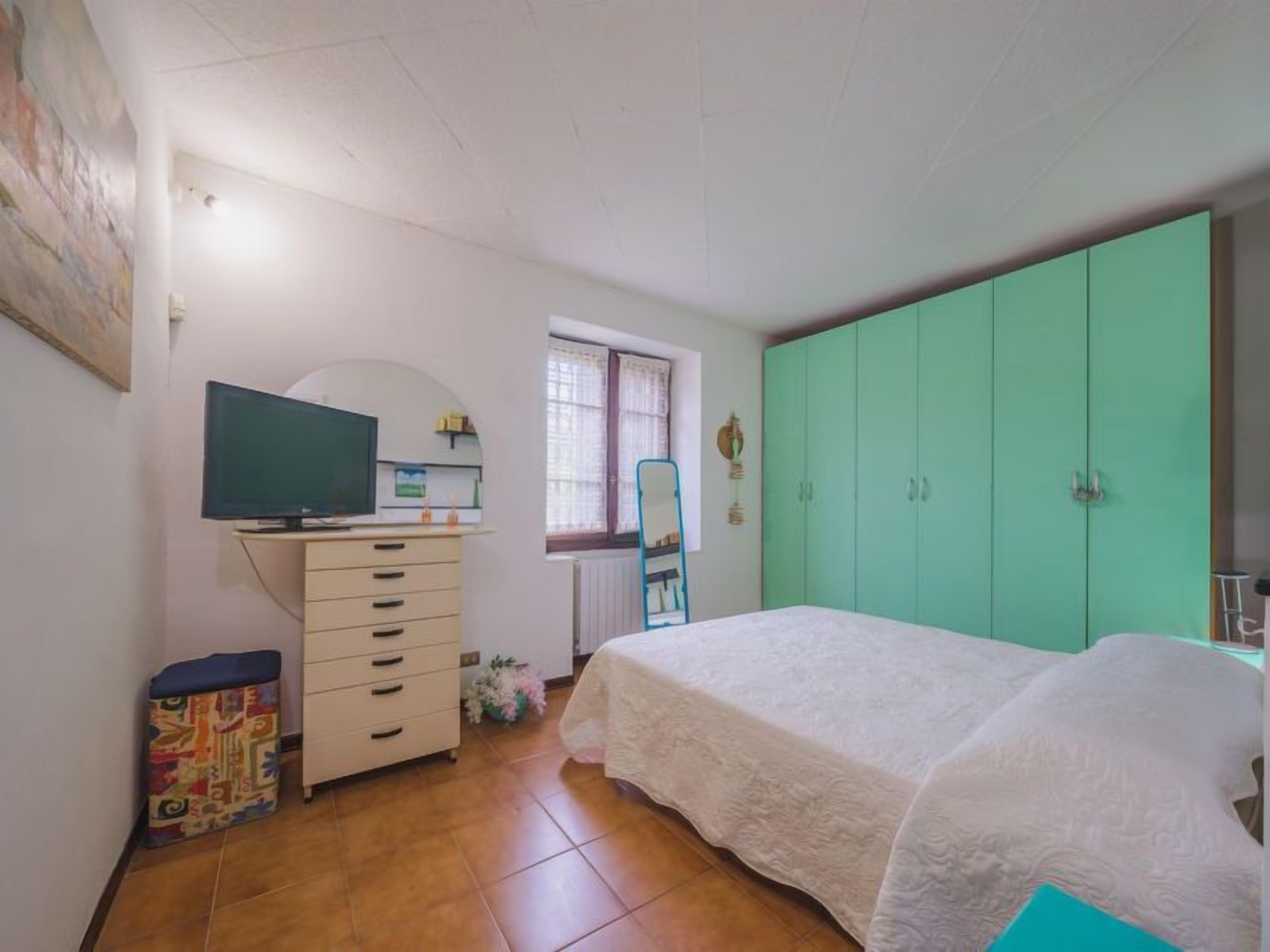 A bedroom with a bed, a dresser, a television, and a window.