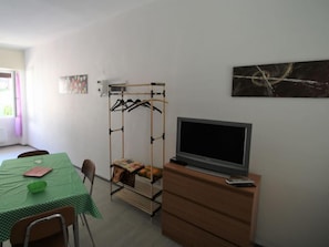 A room with a green checkered table, a wooden TV stand, a coat rack, and a painting on the wall.