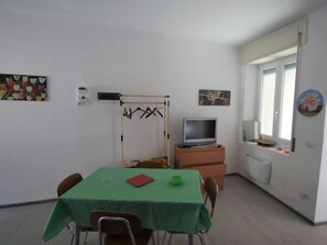 A room with a green checkered table, a television on a wooden cabinet, and a window with a view.