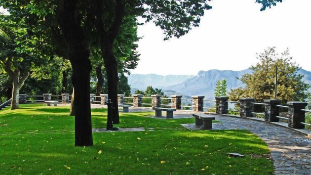 Un parc avec des bancs en pierre, un sentier en pierre et des arbres.