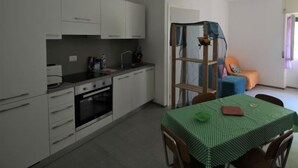 Une cuisine de taille réduite, avec des meubles blancs, un évier et une table à manger recouverte d’une nappe verte.