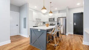 Una cocina moderna con gabinetes blancos, electrodomésticos de acero inoxidable y una isla central con taburetes de bar.