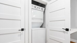 Un lavadero con lavadora y secadora de carga frontal, puertas blancas y piso de madera.
