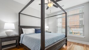 Una cama con dosel de madera y una colcha azul claro, con mesitas de noche y lámparas a cada lado, en una habitación con ventanas amplias y vistas al exterior.