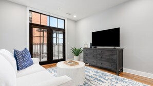 Una sala de estar moderna con un sofá blanco, un aparador de madera oscura, un televisor de pantalla plana y una alfombra estampada.