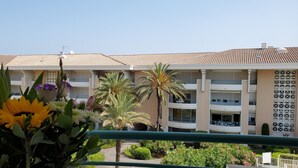 A multi-story hotel with balconies, a tiled roof, and a garden area with flowers and palm trees.