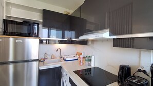 A compact kitchen with a stainless steel refrigerator, a microwave, a sink with a faucet, a toaster, and a black coffee maker.