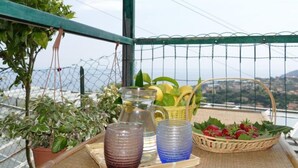 Un balcón con plantas en macetas, una cesta de mimbre con fresas y dos recipientes de vidrio sobre una bandeja.