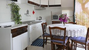 Cocina compacta con armarios blancos, un lavamanos, una estufa y un comedor con mesa y sillas.