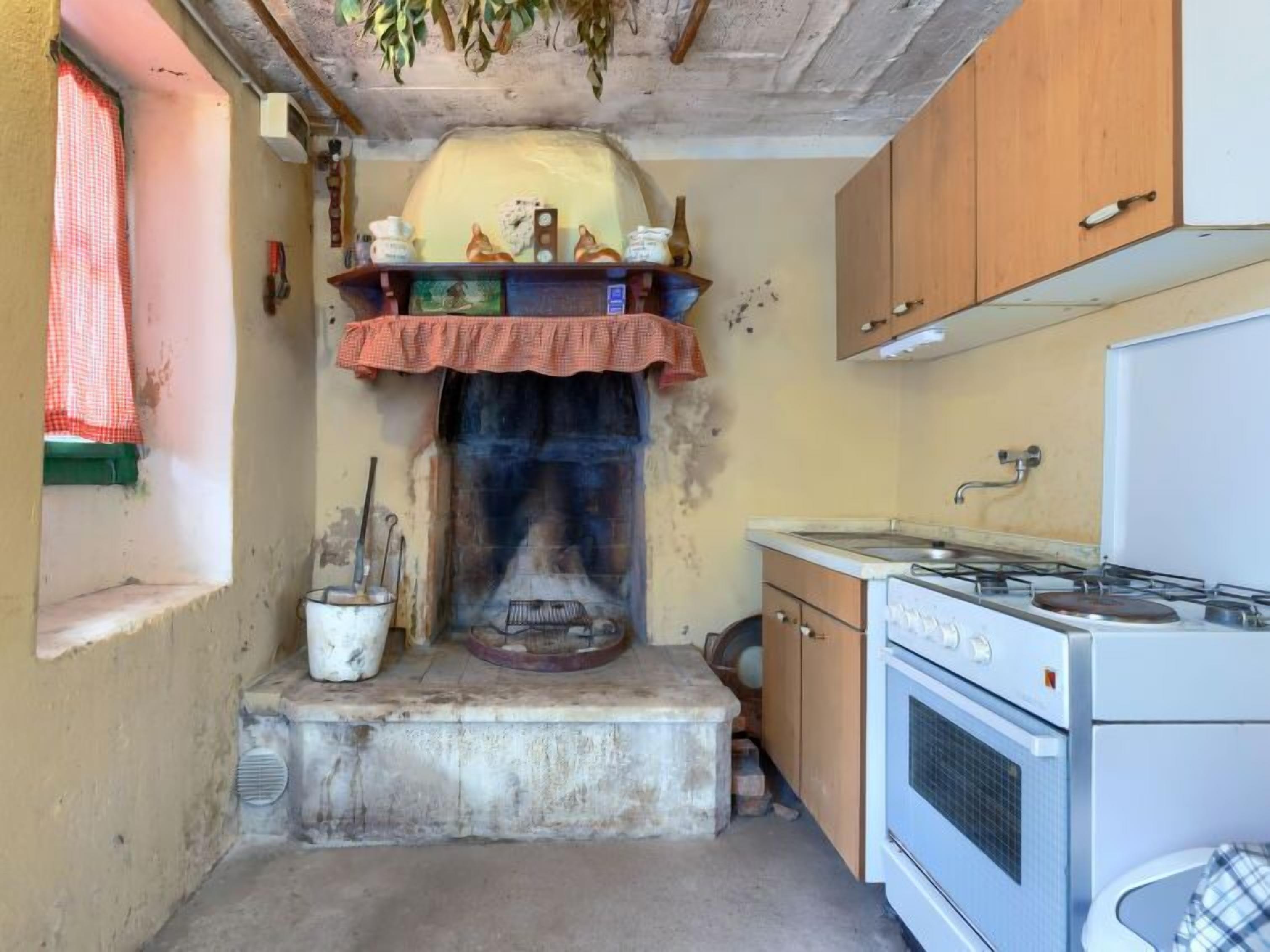 Een kleine keuken met een fornuis, een spoelbak en een klein raam met een rode gordijn.