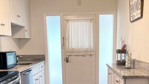 Una cocina con armarios blancos, microondas, horno y pileta.