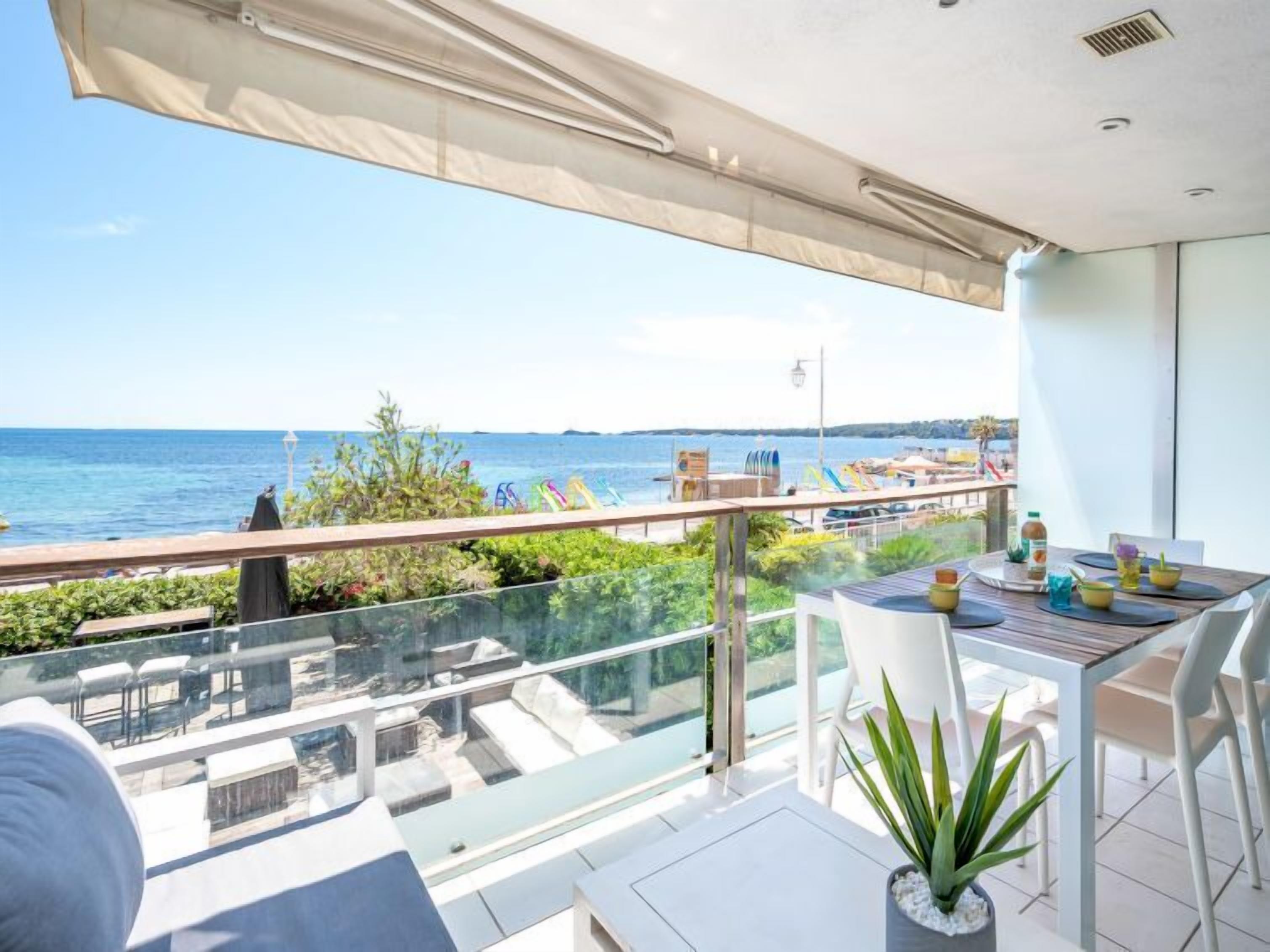 A balcony with a view of the sea, a table with chairs, and a potted plant.