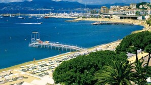 Una marina costera con barcos, un muelle y una playa con tumbonas.