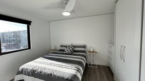 A bedroom with a bed, a window, a wardrobe, and a bedside table.