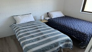 A small, single-bed room with a white brick wall, a wooden nightstand, and a window.