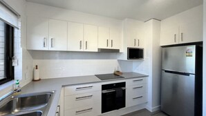 A modern kitchen with white cabinets, stainless steel appliances, and a black oven. - Modern Kings Beach: Walk to Beach (CALOUNDRA)