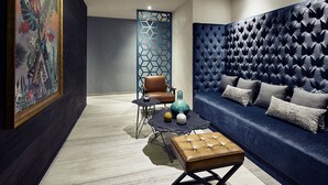 Una sala de estar moderna con un sofá azul oscuro, un otoman de cuero marrón, una pared con estampado azul y un jarrón decorativo sobre una mesita.