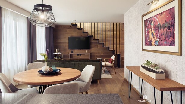 Ein modernes Wohnzimmer mit einem runden Holzes Esstisch, einer Couch und einem an der Wand montierten Fernseher.