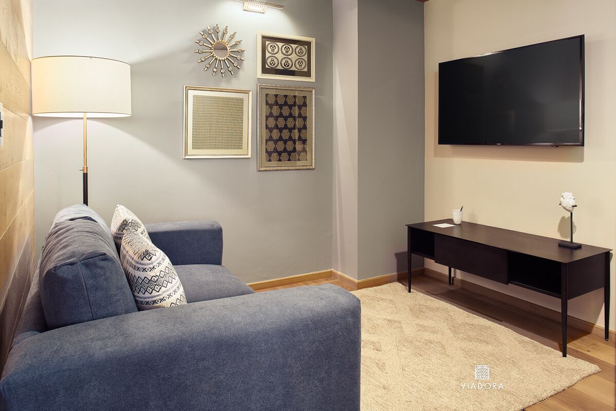 En moderne stue med en grå sofa, et sort skrivebord og et ophængt fjernsyn.