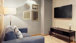 Ein modernes Wohnzimmer mit einem grauen Sofa, einem schwarzen Schreibtisch und einem an der Wand befestigten Fernseher.