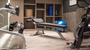 Ein Fitnessraum mit Trainingsgeräten, einer Bank und Regalen mit Gegenständen.