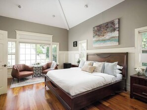 Une chambre à coucher avec un grand lit, une chaise, une table de chevet et un tableau au mur.