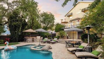 A swimming pool with lounge chairs and umbrellas, surrounded by trees and a building with a balcony.