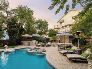 Une piscine entourée d’arbres et d’un bâtiment doté d’un balcon, avec des chaises longues et des parasols à proximité.