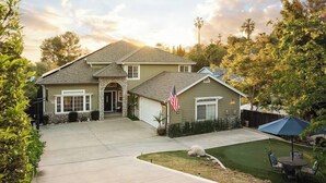 A two-story house with a stone archway entrance, a garage, and a well-maintained lawn. - 5br Home with Pool, Hot Tub, BBQ, Putting green (La Mesa)