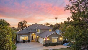 A two-story house with a stone entrance, a driveway, and a well-maintained lawn. - 5br Home with Pool, Hot Tub, BBQ, Putting green (La Mesa)