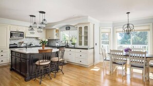 A spacious kitchen with a central island, bar stools, and a dining area with a table and chairs. - 5br Home with Pool, Hot Tub, BBQ, Putting green (La Mesa)