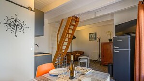 A dining area with a wooden table set for two, a ladder against the wall, a black refrigerator, and a television. - Maison Des Lilas by Interhome (Quiberon)