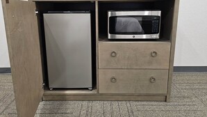 A compact kitchenette with a built-in refrigerator and microwave, and a coffee maker on top. - Bunkhouse Lodge (Seadrift)