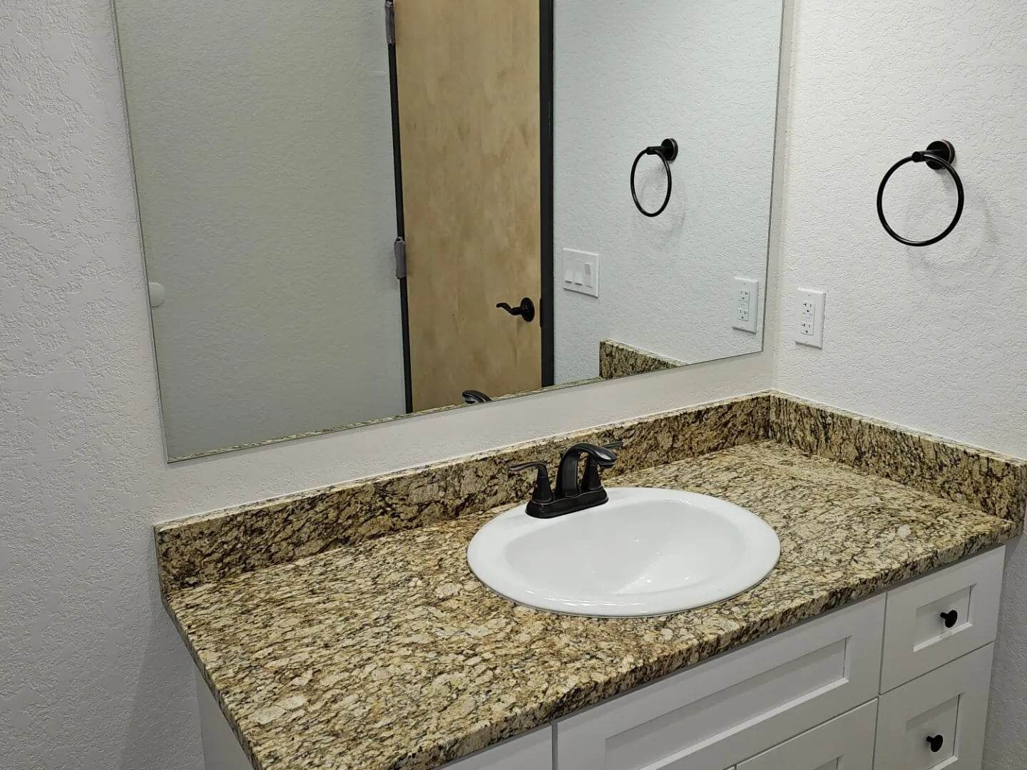 A bathroom with a granite countertop, a white sink, and a mirror.