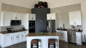 A kitchen with white cabinets, granite countertops, stainless steel appliances, and a brick accent wall. - Bunkhouse Lodge (Seadrift)