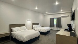 A hotel room with two beds, a desk, a flat-screen TV, and a window with curtains. - Bunkhouse Lodge (Seadrift)