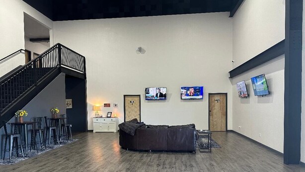 A spacious lobby with a wooden floor, a staircase, a sofa, a dining area, and three mounted televisions. - Bunkhouse Lodge (Seadrift)