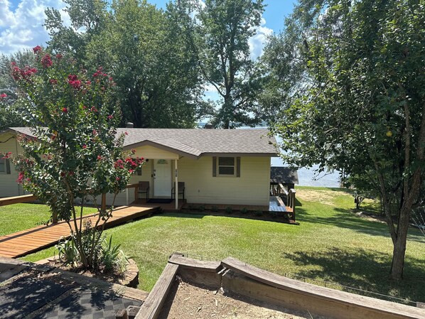 A small, single-story cabin with a porch, a deck, and a view of a lake. - Peaceful lake front home with wrap around porch and relaxing views! (Farmerville)