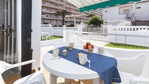 A balcony with a table set for breakfast, overlooking a residential area with white buildings and a green lawn. - Peñismar Garden by Interhome (Peñiscola)
