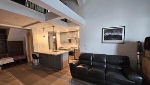Una cocina moderna con una isla central, un comedor con banco y un sofá de cuero negro.