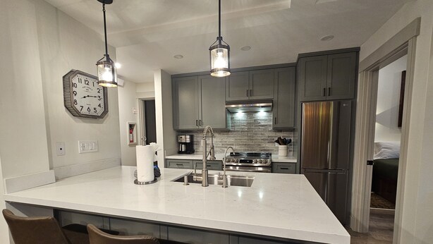 Una cocina moderna con una isla grande, taburetes de bar, electrodomésticos de acero inoxidable e iluminación colgante.
