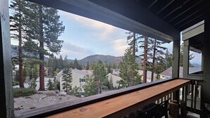 Una terraza de madera con vista a una zona residencial, árboles y montañas.