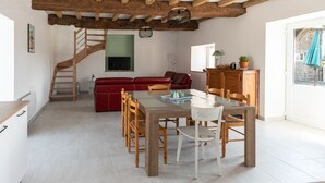 A spacious living area with a dining table, red sofa, wooden staircase, and a view of the outside. - Gîtes Ti Tud-kozh, Location "L' Arguenon" (PLUDUNO)
