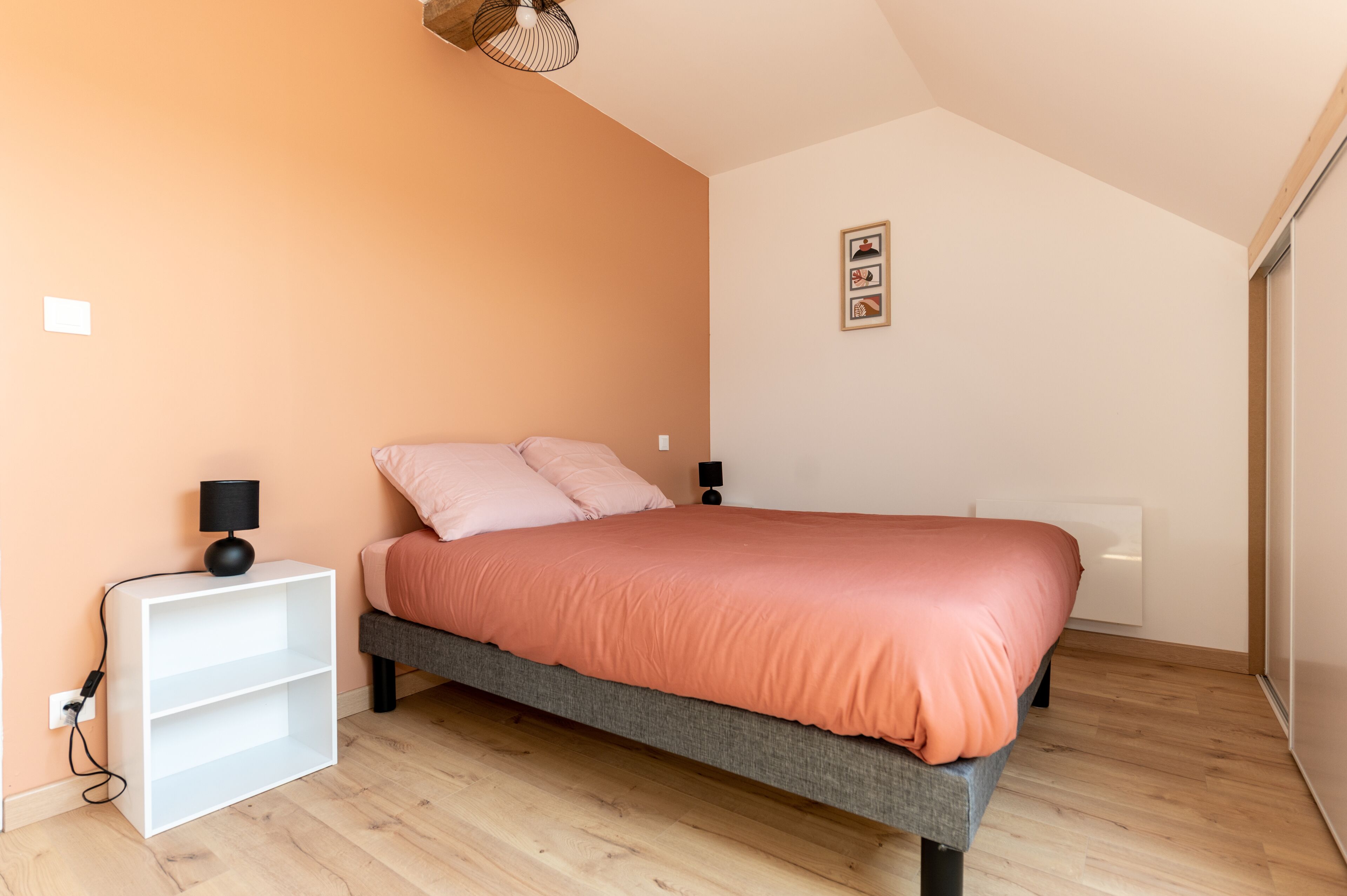 A bedroom with a bed, a white nightstand, a lamp, and a ceiling light.