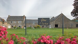 A fenced area with a sign reading "Gites Ti Tud-Kozh" and a building with stone walls in the background. - Gîtes Ti Tud-kozh, Location "L' Arguenon" (PLUDUNO)