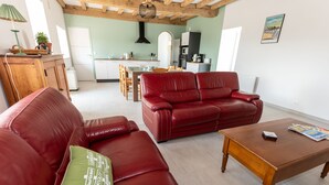 A living room with a red leather sofa, a wooden coffee table, and a kitchen in the background. - Gîtes Ti Tud-kozh, Location "L' Arguenon" (PLUDUNO)