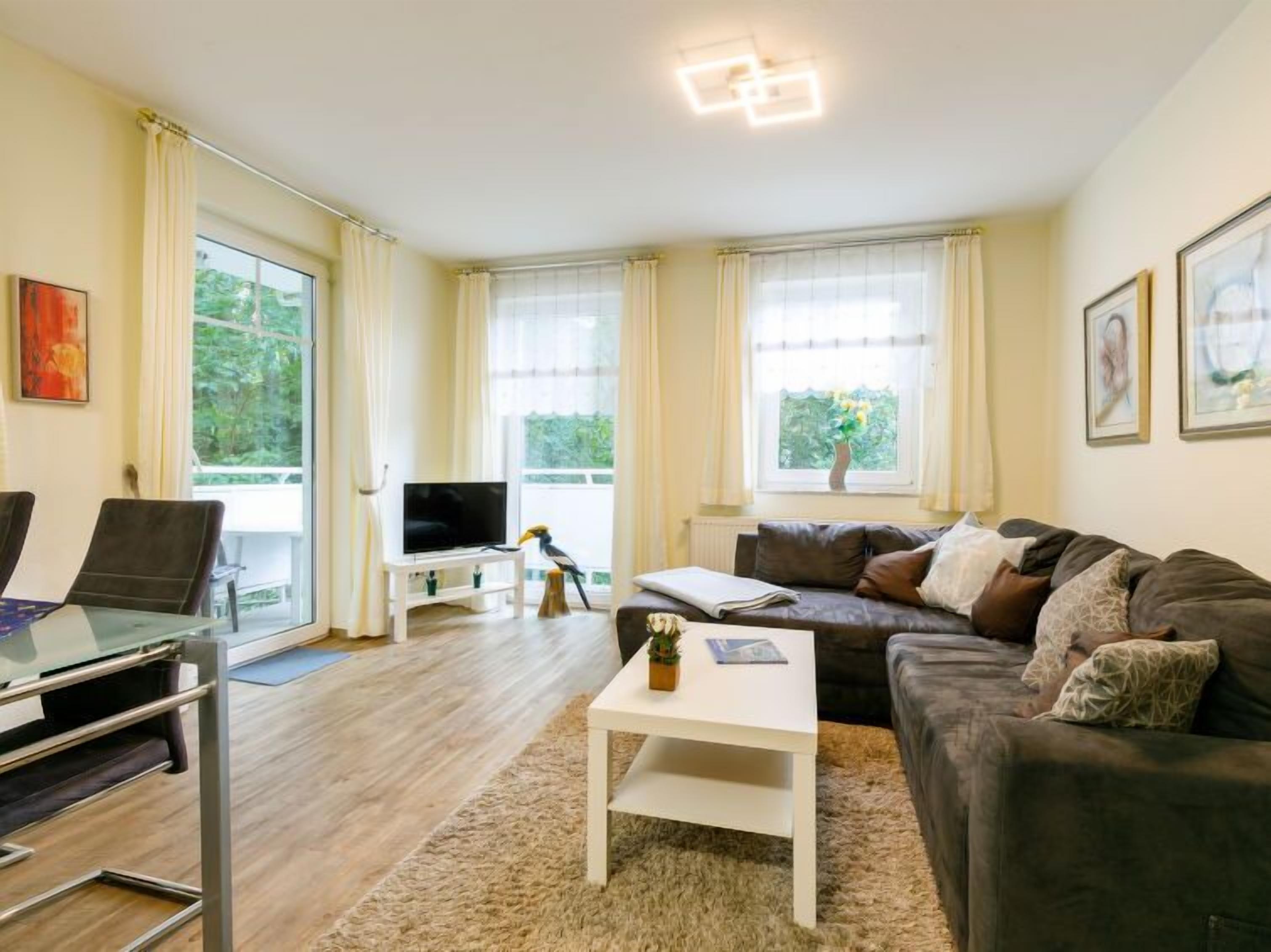 Ein modernes Wohnzimmer mit Sofa, Couchtisch, Fernseher und einem Essbereich mit Stühlen.